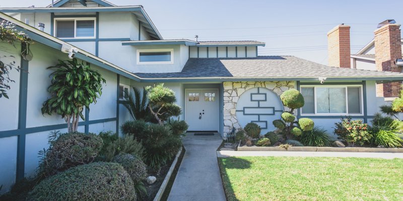 A charming home with a neatly manicured garden, unique geometric stone accents, and a welcoming pathway leading to the front door.