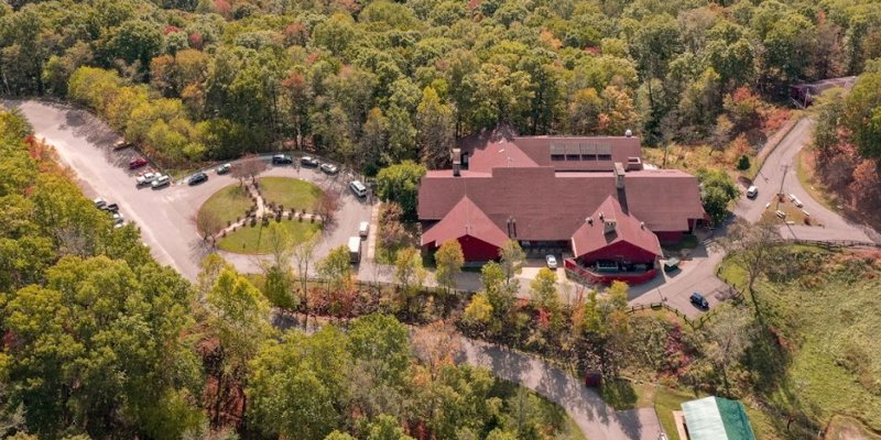 An aerial view of a large facility nestled in a lush, forested area, with winding roads, ample parking, and a serene, natural setting.