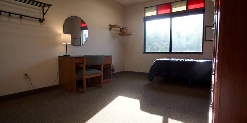 A bright, minimalist bedroom with natural light, simple furnishings, and a cozy bed, offering a calm and peaceful space for rest.