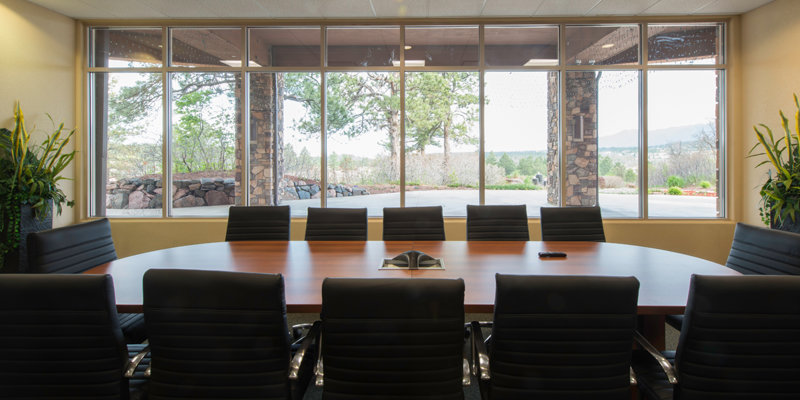 A professional conference room with a large table, comfortable chairs, and a wall of windows offering a view of the natural surroundings.