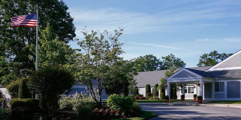 A well-maintained building surrounded by lush greenery, featuring an American flag waving in the breeze. A peaceful and welcoming environment.