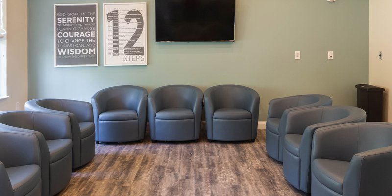 A spacious room arranged with comfortable, modern chairs in a circle. Inspirational wall art and a TV create a welcoming setting for group sessions.