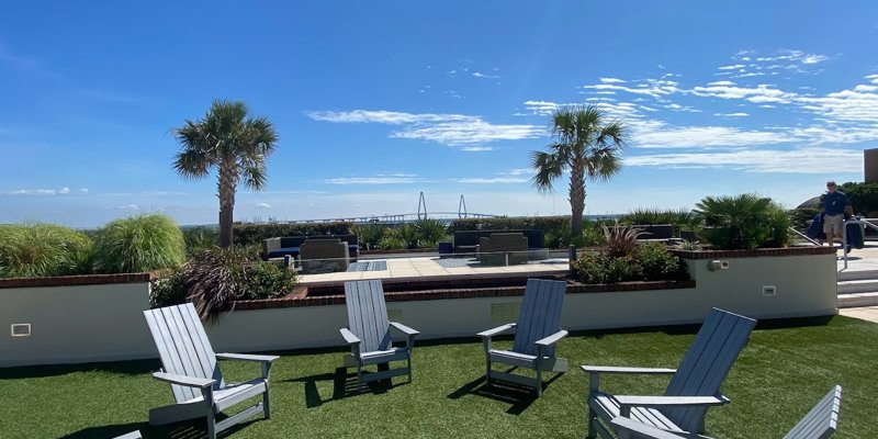 Scenic outdoor patio with Adirondack chairs, lush greenery, and palm trees, offering a relaxing space with beautiful views of a distant bridge.