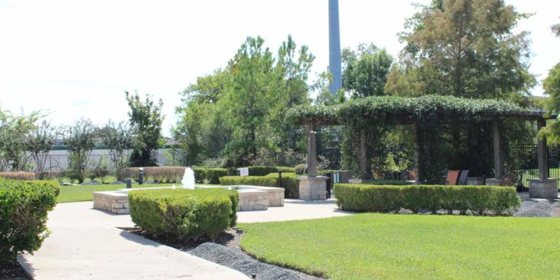 A beautifully landscaped garden with a peaceful fountain, shaded seating area under a vine-covered pergola, and well-maintained greenery.