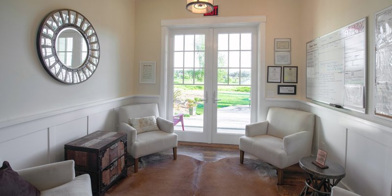 A cozy waiting area with comfortable armchairs, a large mirror, and a bright view through glass doors, creating a welcoming atmosphere.