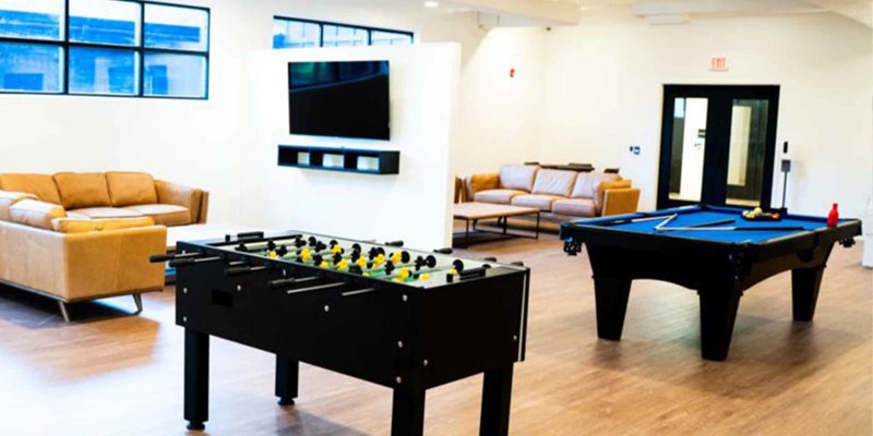 Bright and inviting recreation room with comfortable seating, a pool table, and foosball, perfect for relaxation and socializing.