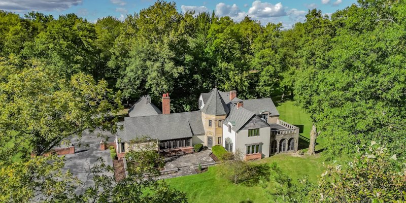 Aerial view of a beautiful estate surrounded by lush greenery, featuring unique architecture and spacious grounds, offering a serene retreat.