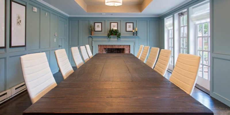 A sophisticated conference room featuring a long wooden table, elegant white chairs, and classic decor, creating a professional and inviting space for meetings.