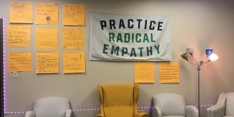 A cozy room with soft chairs, motivational posters, and a large banner saying "Practice Radical Empathy," creating a warm, supportive space.