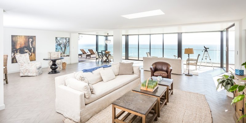 Spacious living room with coastal views, cozy seating, natural light, and seamless access to a balcony overlooking the ocean horizon.