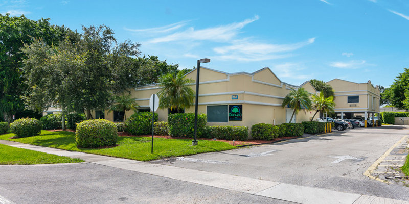  A bright, inviting building with palm trees and neatly trimmed bushes, set against a clear blue sky. The parking lot is accessible and well-maintained.