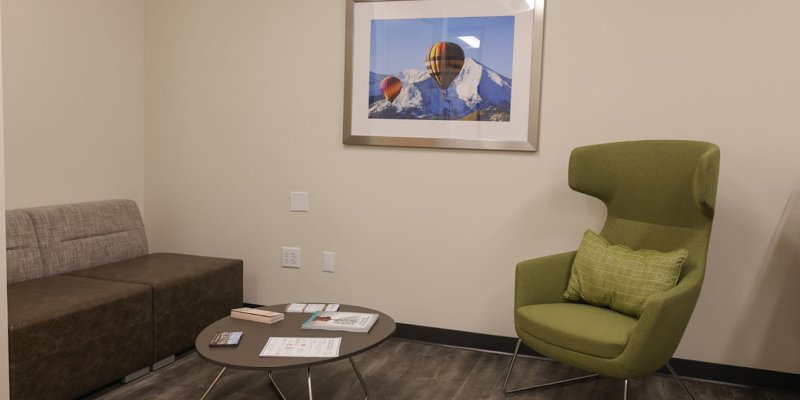 A cozy seating area featuring a green modern chair, a small table with brochures, and artwork of hot air balloons over mountains on the wall.