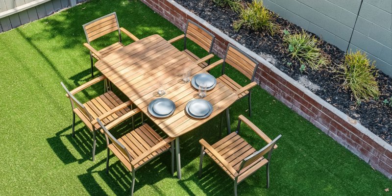 A cozy outdoor dining area with a wooden table and six matching chairs, set on a lush green lawn, perfect for enjoying meals in nature.