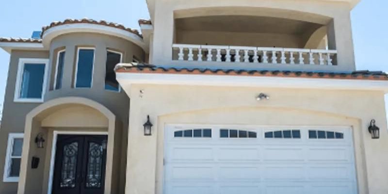  A beautiful, two-story home with a Mediterranean-style design, featuring a balcony, arched windows, and a large garage with elegant double doors.