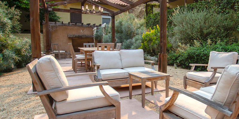 A tranquil outdoor seating area with cushioned wooden chairs under a pergola, surrounded by lush greenery and scenic hillside views, perfect for relaxation.