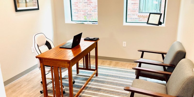 A cozy, well-lit office space with a wooden desk, comfortable chairs, and natural light from two windows. A welcoming environment for meetings.