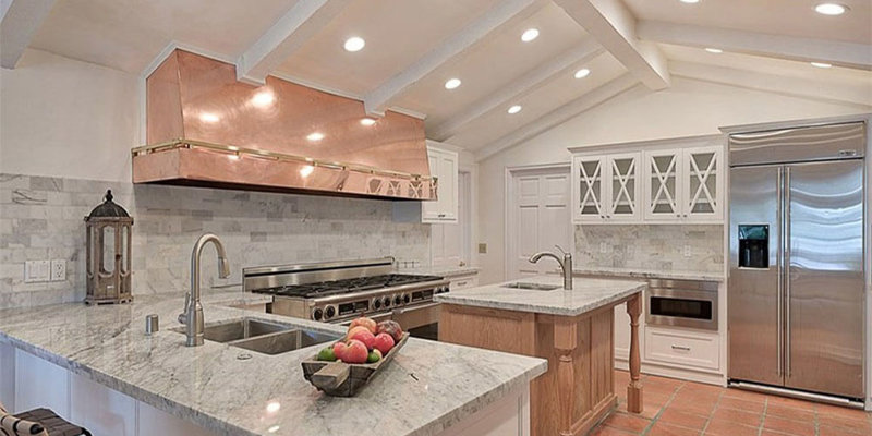 A bright and spacious kitchen with marble countertops, a copper range hood, stainless steel appliances, and a central island, exuding luxury and warmth.