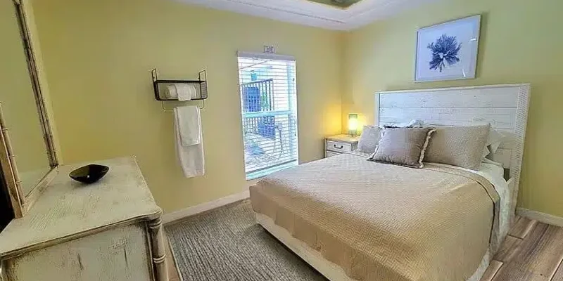 A serene bedroom with soft lighting, a cozy bed with neutral bedding, a vintage-style dresser, and natural light streaming through a window.