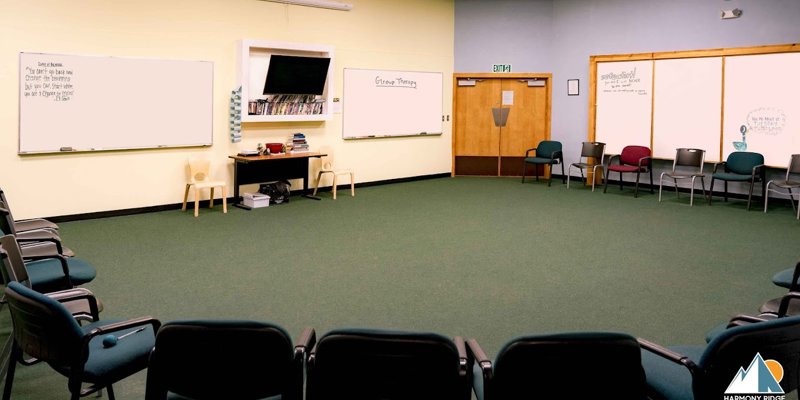 A spacious, welcoming group therapy room with arranged chairs, whiteboards for notes, and calming colors, fostering a supportive environment.