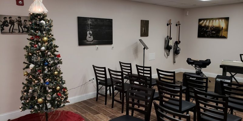 A festive music room decorated with a Christmas tree, guitars on the wall, a keyboard, drum set, and chairs arranged for a cozy performance.