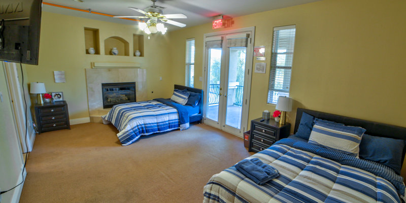 A spacious bedroom with two cozy beds, striped blue bedding, a fireplace, and access to a balcony, creating a peaceful and comfortable atmosphere.