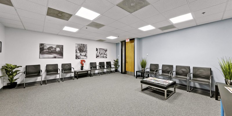 A spacious, well-lit waiting room with modern black chairs, vibrant plants, and artistic wall photos creates a welcoming atmosphere.