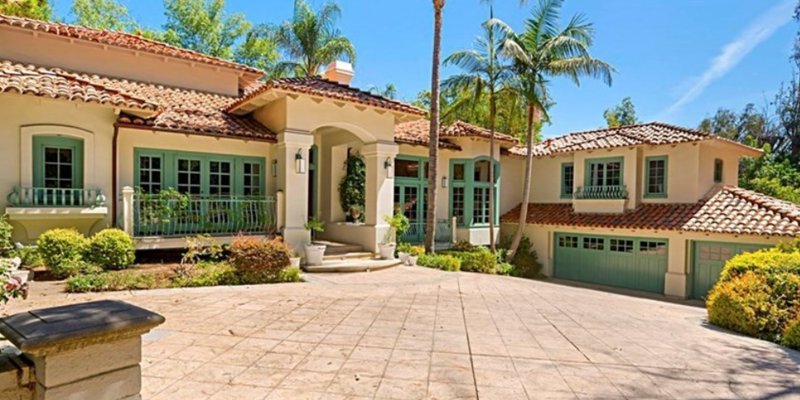 A stunning Mediterranean-style home with a tiled roof, arched entryways, lush landscaping, and palm trees, offering a bright and serene atmosphere.