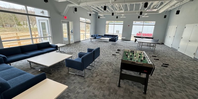 A spacious recreational room filled with natural light, featuring cozy seating areas, foosball, and ping-pong tables, providing a relaxed and social atmosphere.