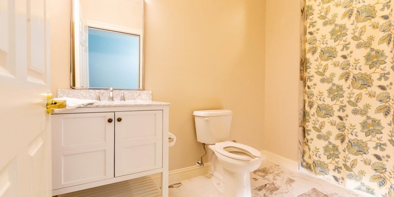 Bright and clean bathroom with a marble-topped vanity, floral shower curtain, large mirror, and elegant tile flooring for a fresh, inviting feel.