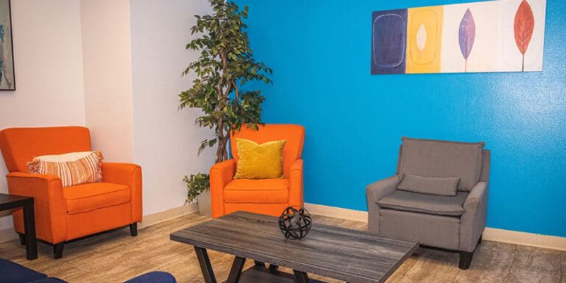 A vibrant and cozy seating area featuring bright orange and gray chairs, a stylish coffee table, and a blue accent wall with modern art.