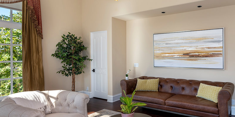  Elegant living room with a plush leather sofa, cozy armchair, large windows, decorative chandelier, and tasteful artwork, creating a warm and inviting space.