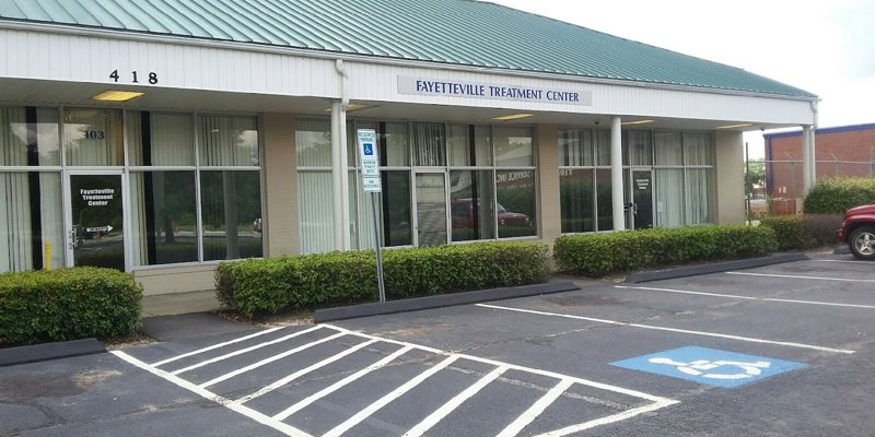 The exterior of Fayetteville Treatment Center with large windows, a reserved parking spot for accessibility, and a neatly landscaped entrance.