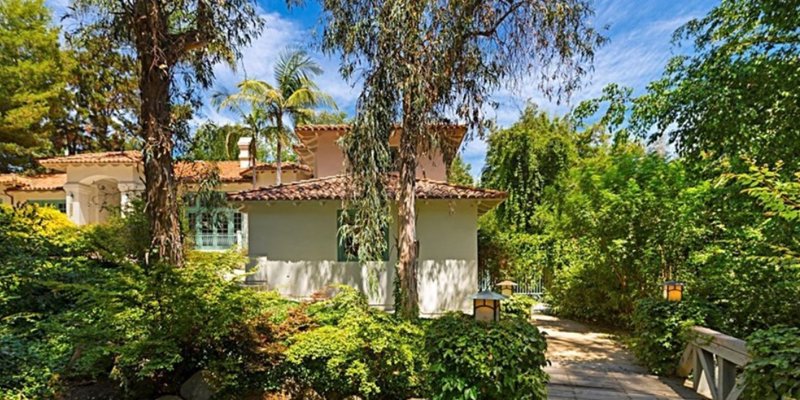 A peaceful Mediterranean-style home surrounded by lush greenery, with a charming walkway and soft natural light filtering through the trees.