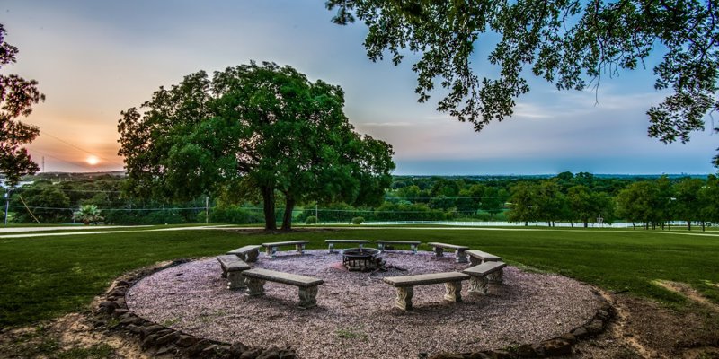 Serene sunset view over a peaceful fire pit area surrounded by benches, offering a tranquil space for reflection and connection.