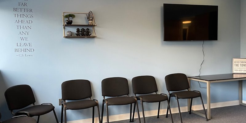 A calm waiting area with neatly arranged chairs, a motivational quote by C.S. Lewis on the wall, a decorative shelf, and a mounted TV for comfort.