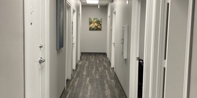 A well-lit hallway with sleek wood-patterned floors and white doors on either side. Artworks on the walls add a welcoming touch to the space.