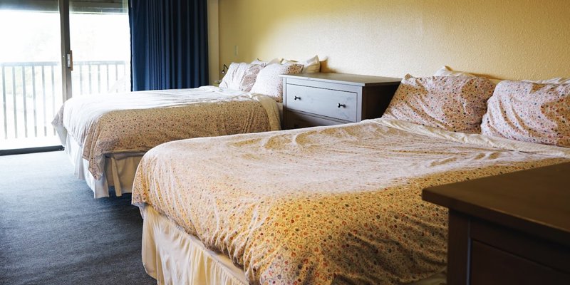 A cozy room featuring two comfortable queen beds with floral bedding, soft lighting, a private balcony, and dark blue curtains.