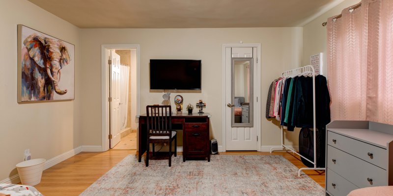 Bright, cozy room featuring a wooden desk, wall-mounted TV, and a clothes rack, offering a comfortable and organized living space.