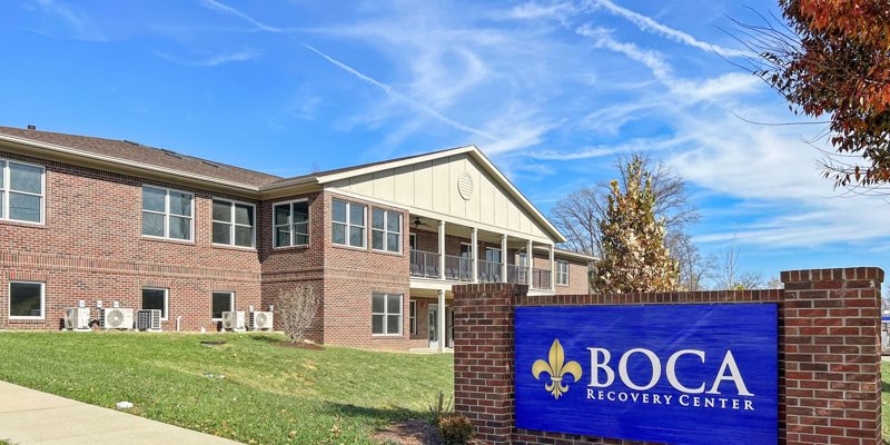 Boca Recovery Center's brick building, surrounded by greenery, with a welcoming sign and a clear blue sky, creates a serene atmosphere.