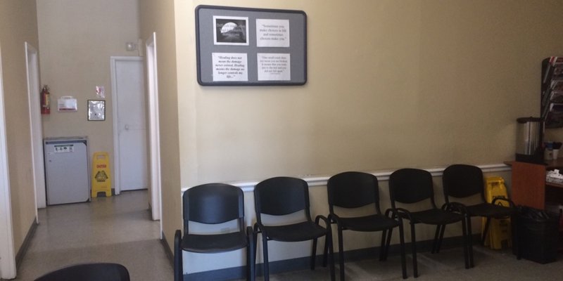 A simple waiting area with black chairs, a coffee station, and motivational quotes on the wall. The space is clean and welcoming for visitors.