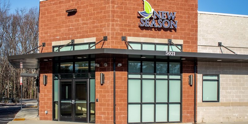 A bright, modern building with large windows and a welcoming entrance, featuring a sign for New Season, standing against a clear sky.