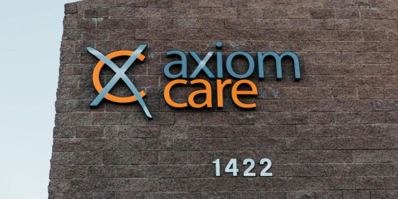 The exterior view of a building shows the Axiom Care logo in orange and blue on a brick wall, along with the address number 1422.