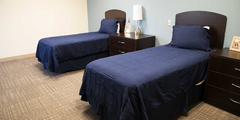 A cozy, well-lit bedroom with two neatly made twin beds featuring dark wood headboards and matching bedside tables, creating a calm atmosphere.