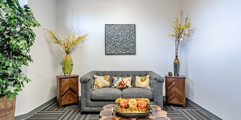 A cozy seating area featuring a modern gray sofa, accent pillows, and stylish wood furniture, complemented by decorative plants and artwork.