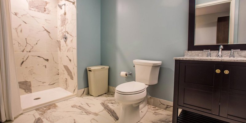 Modern bathroom with marble-tiled shower and floors, a sleek vanity, and soft blue walls, offering a clean and elegant space for relaxation.