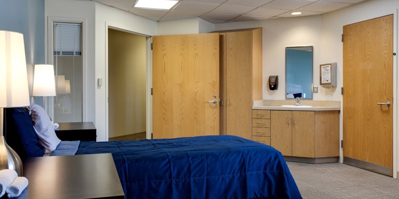 A comfortable bedroom with neatly made beds, blue bedding, soft lighting, wooden furniture, and an in-room sink, providing a clean and relaxing space.