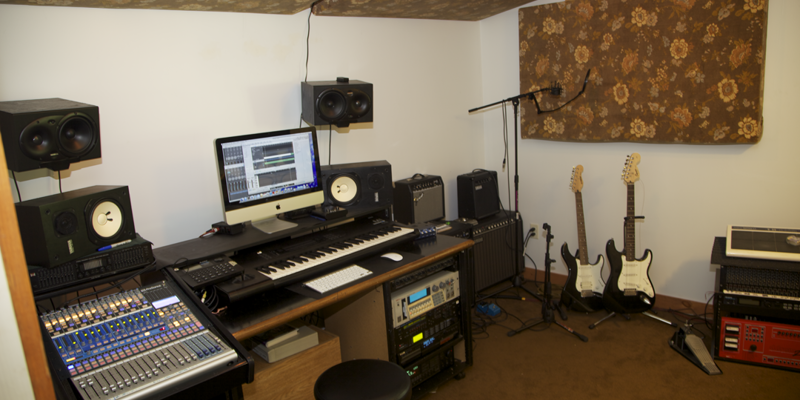 A cozy recording studio with professional equipment, including a keyboard, speakers, and guitars, perfect for creative music production.