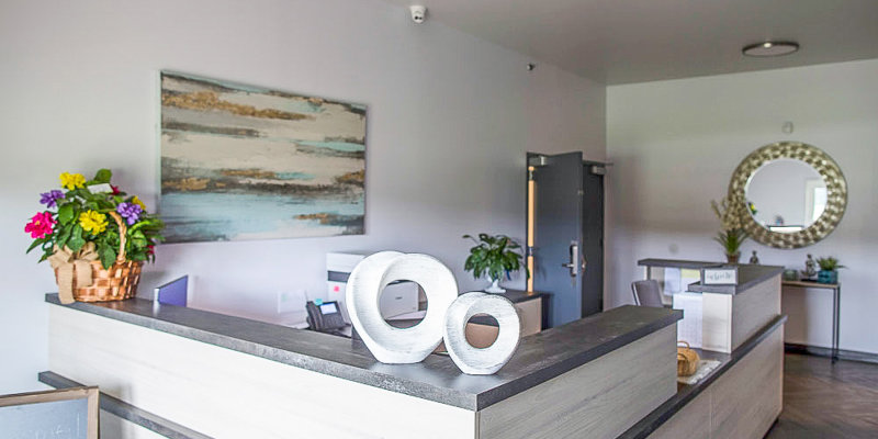 A welcoming reception area with modern decor, including fresh flowers, abstract artwork, and a decorative circular mirror, creating a calm atmosphere.