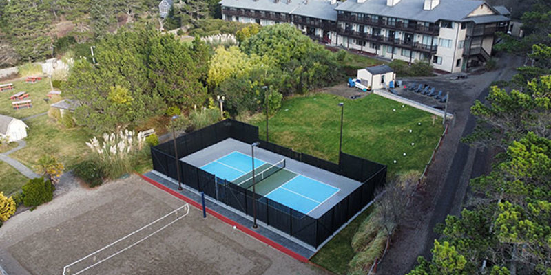 Aerial view of a resort featuring a well-maintained pickleball court, sand volleyball court, and surrounding lush greenery and paths.