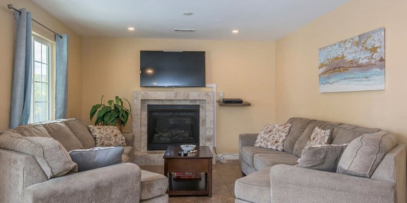 A cozy living room with plush sofas, a fireplace, wall-mounted TV, and soft lighting, creating a warm and inviting space for relaxation.